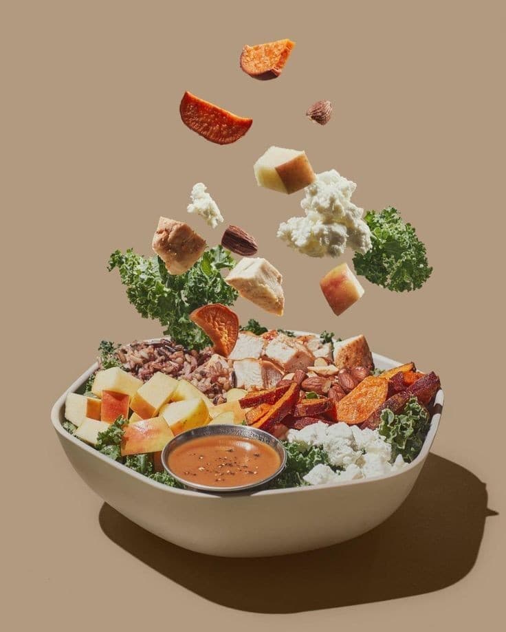 A bowl of salad with ingredients falling into it